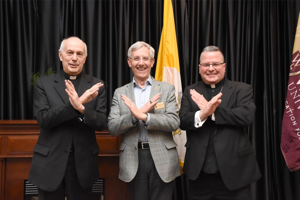 photo of President Collins, Archbishop Caccia, and Bishop Bonnar making swords up hand gesture