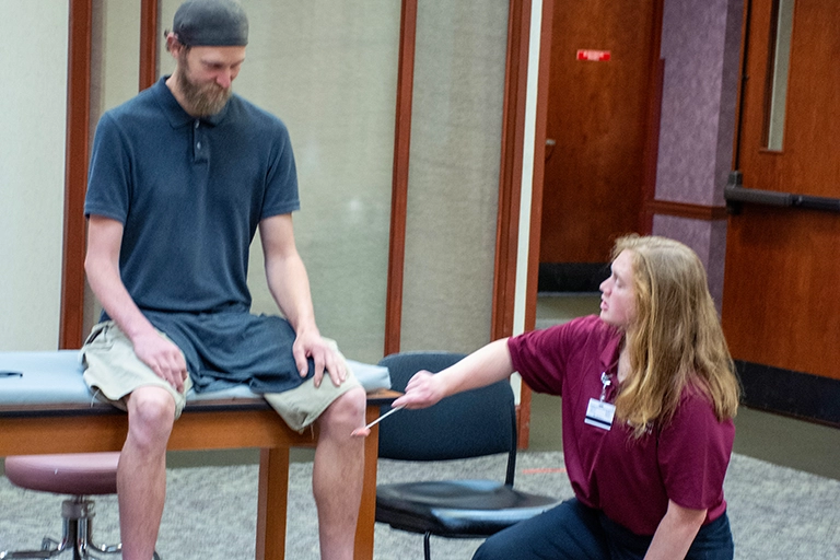 Photo of a Walsh PT student testing a patients knee reflex