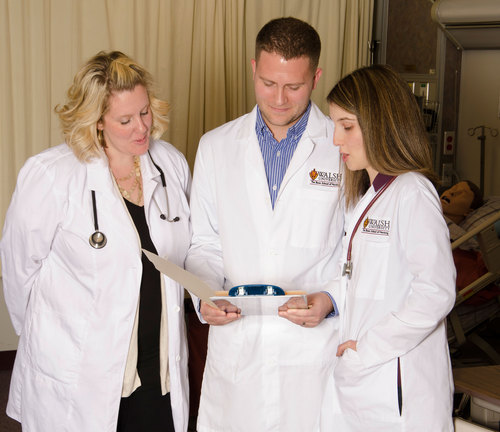 three graduate nursing students in lab coats consulting in an exam room
